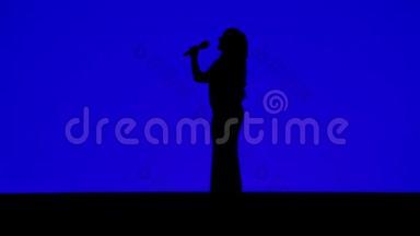 一位<strong>身材</strong>苗条的女歌手在舞台上的<strong>剪影</strong>，蓝色背景上有麦克风